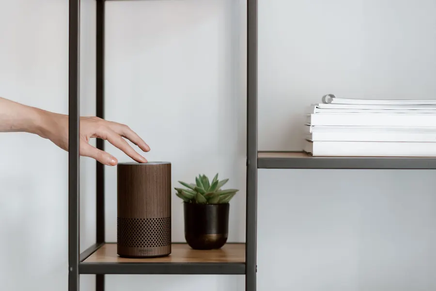 Hand reaching for a voice assistant speaker on a shelf
